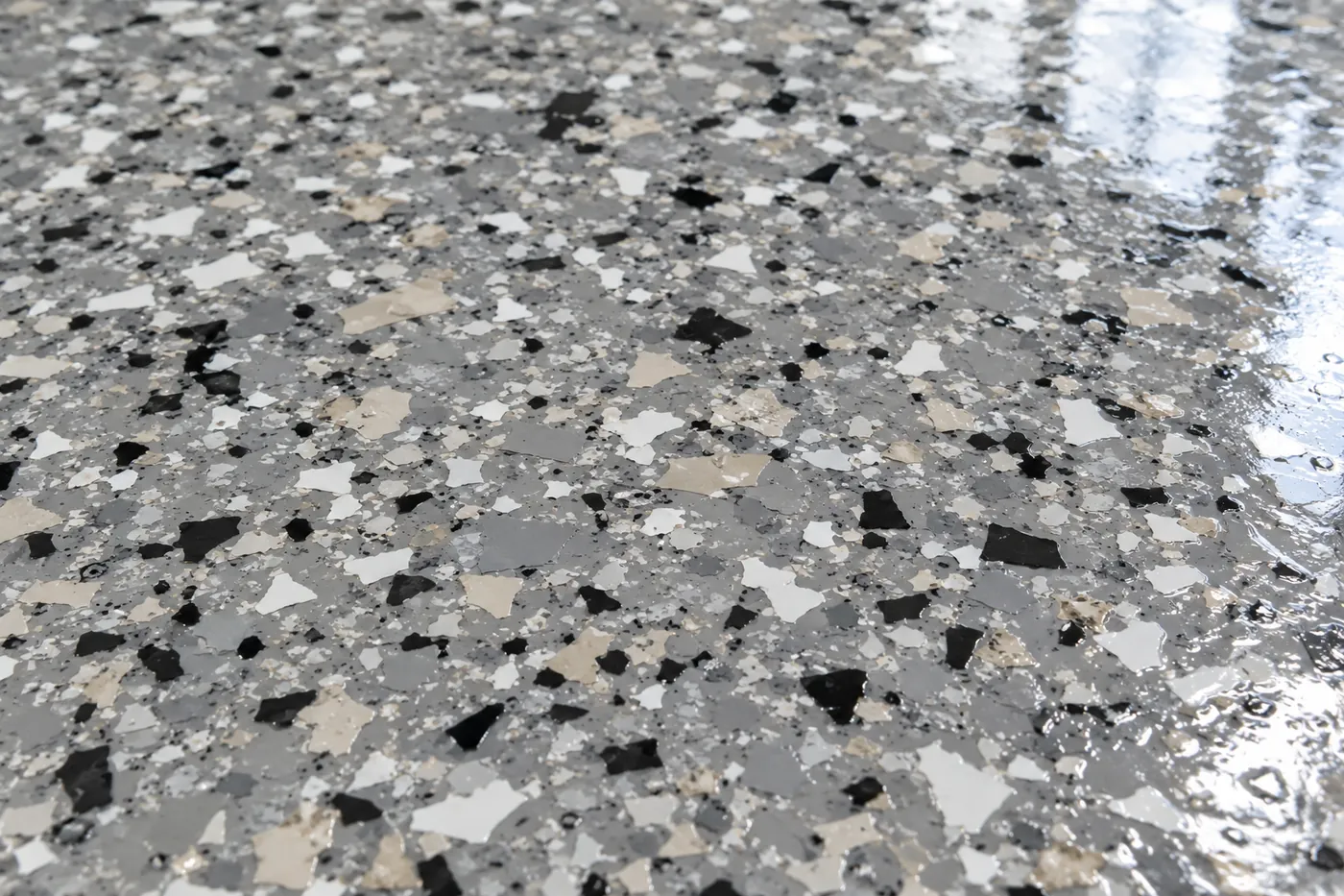 Close-up of grey vinyl flake chips sealed under a glossy polyaspartic topcoat